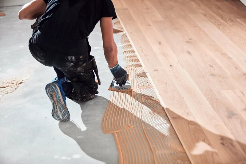 Installer spreading adhesive on a concrete slab beside freshly laid engineered oak planks