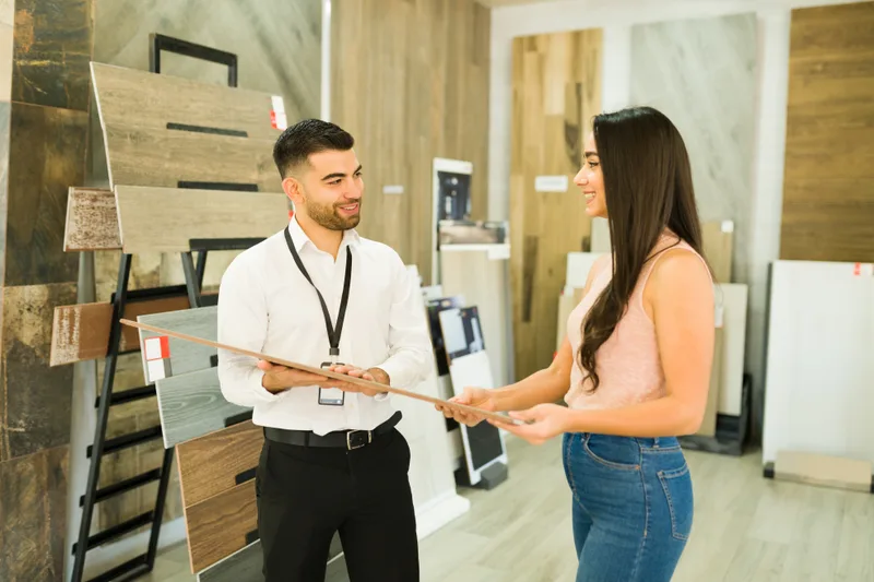 Flooring adviser showing a customer plank samples in front of a wall of wood flooring boards