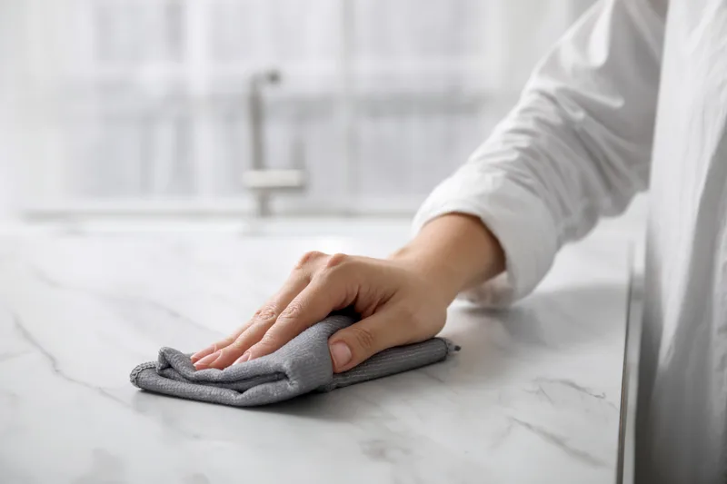 Hand wiping a white marble kitchen counter with a folded grey microfibre cloth