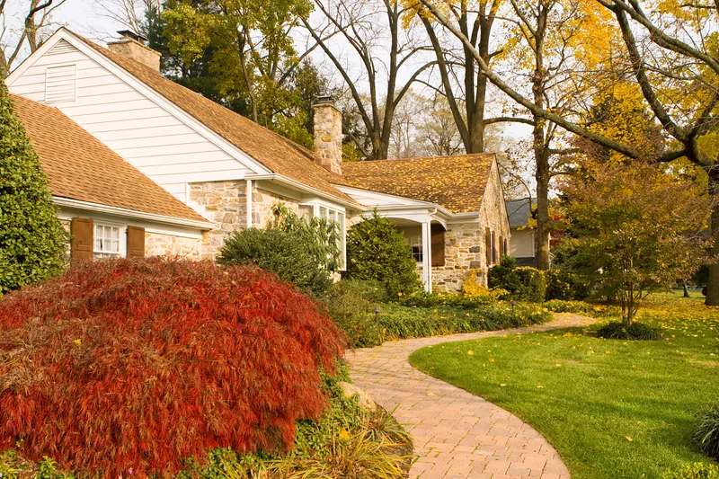 A stone and brick home in autumn with a clean lawn and a curving brick path