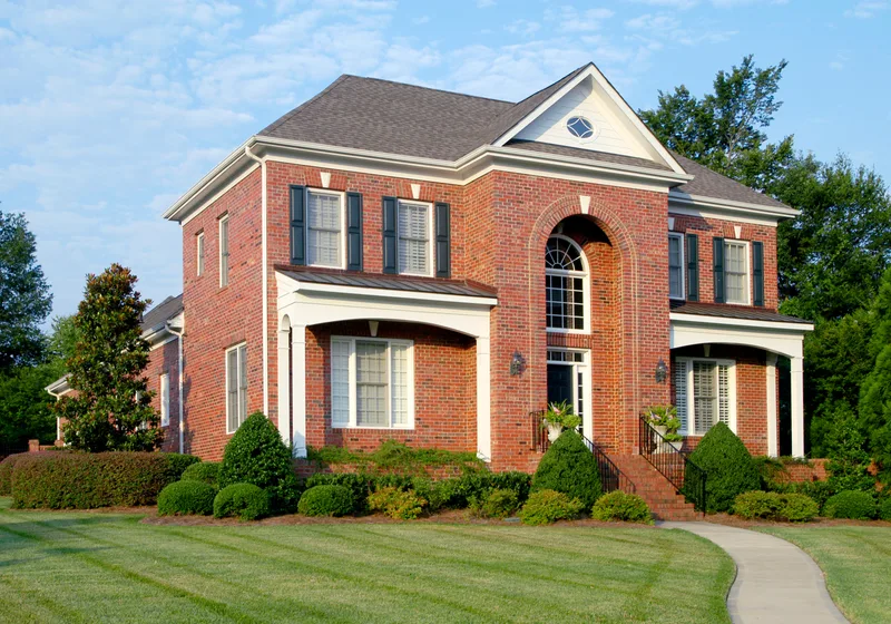 A brick colonial home with a freshly striped front lawn and trimmed shrubs