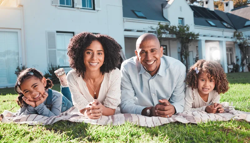 A family of four lying on a blanket on their front lawn, smiling