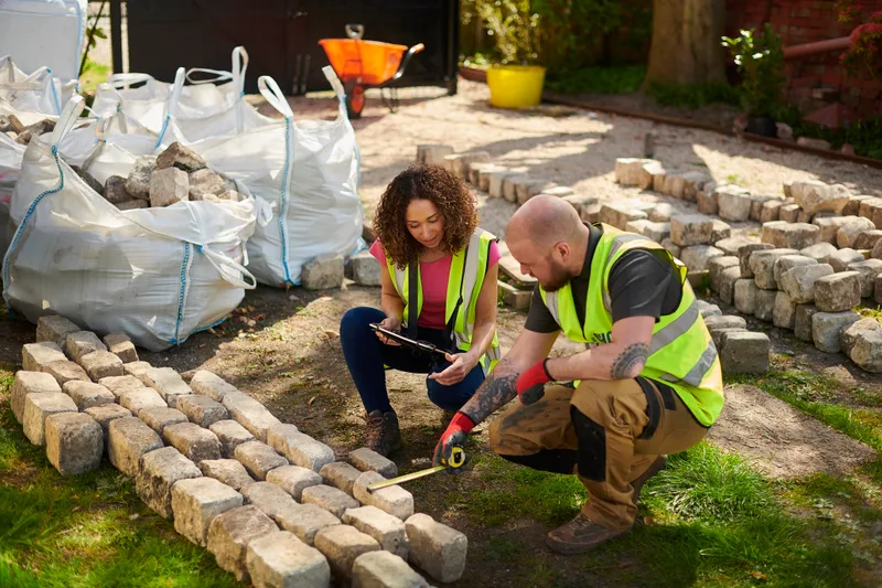 Two Verdant & Co. crew members measuring and setting reclaimed granite setts on site