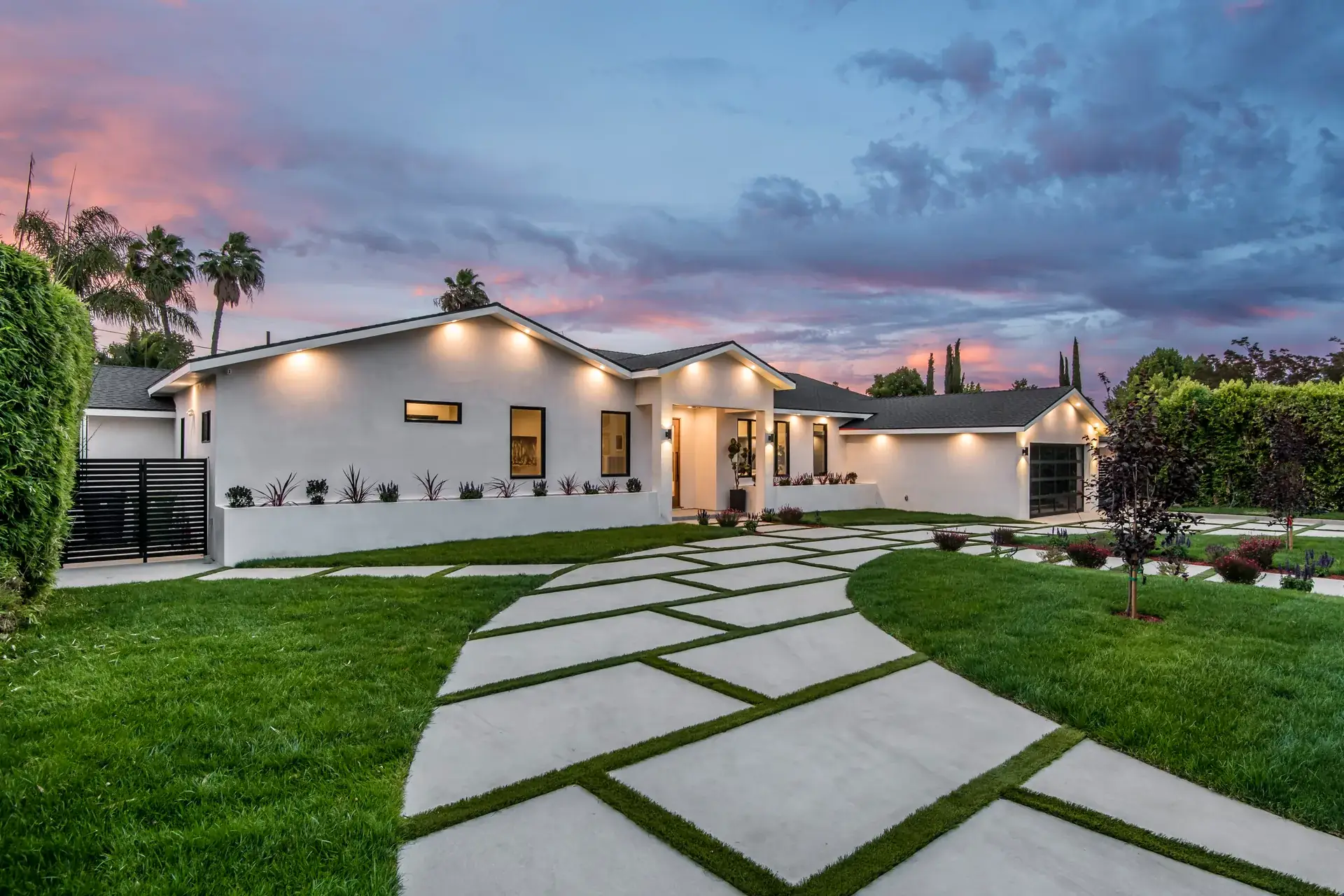 Low white house at sunset behind a curving sweep of oversized pavers set into lawn