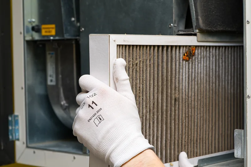 Gloved hand pulling a used furnace filter out of its slot during a tune-up