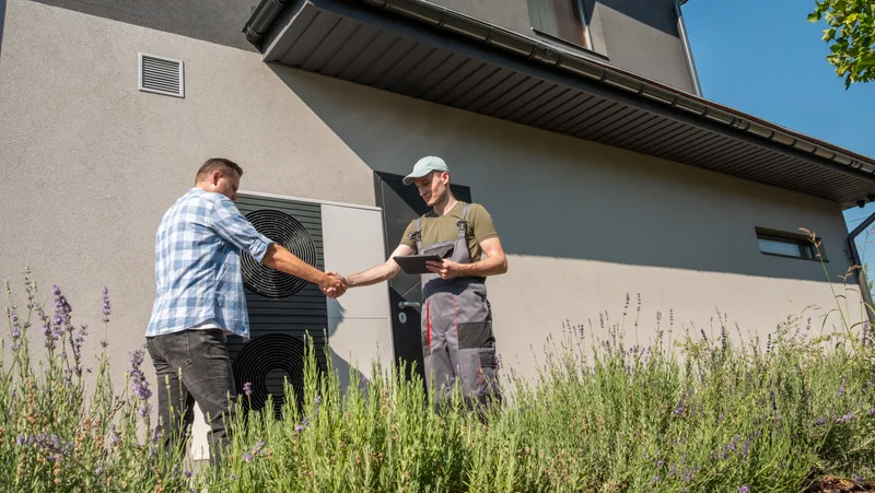Homeowner shaking hands with a technician in front of a house with a new heat pump
