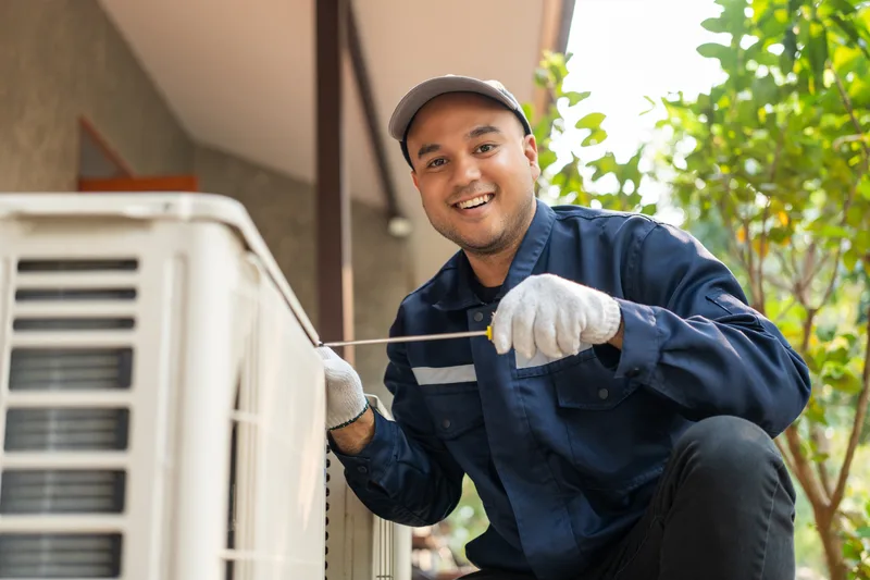 Smiling technician in a navy uniform servicing an outdoor condenser unit