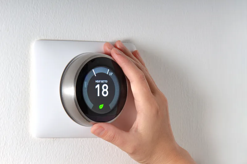 Hand adjusting a round smart thermostat on a white wall
