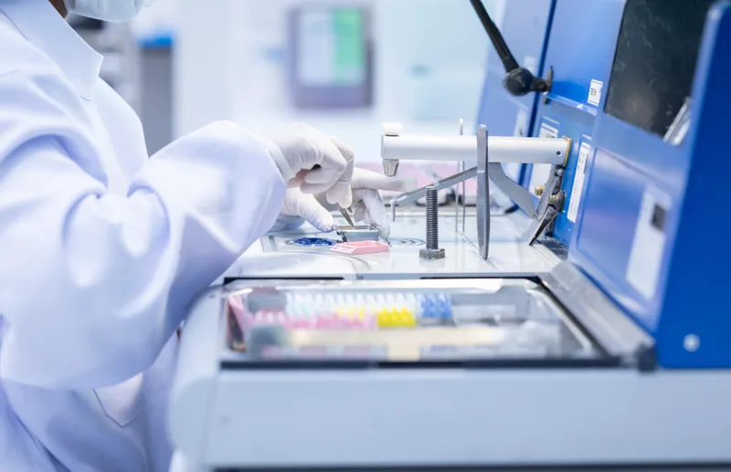 A gloved lab technician preparing samples at an analysis instrument in a clean room