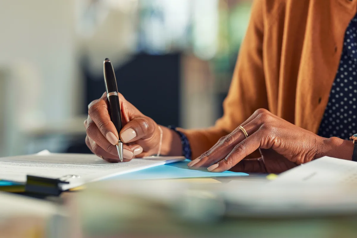 A close-up of a woman's hands signing an application form with a pen