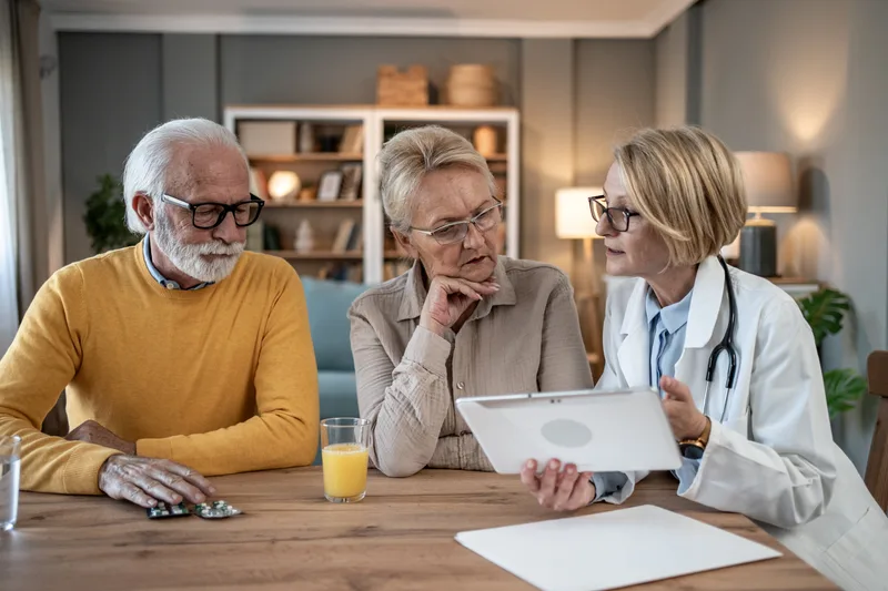 An older couple goes over medical information with a doctor at a kitchen table
