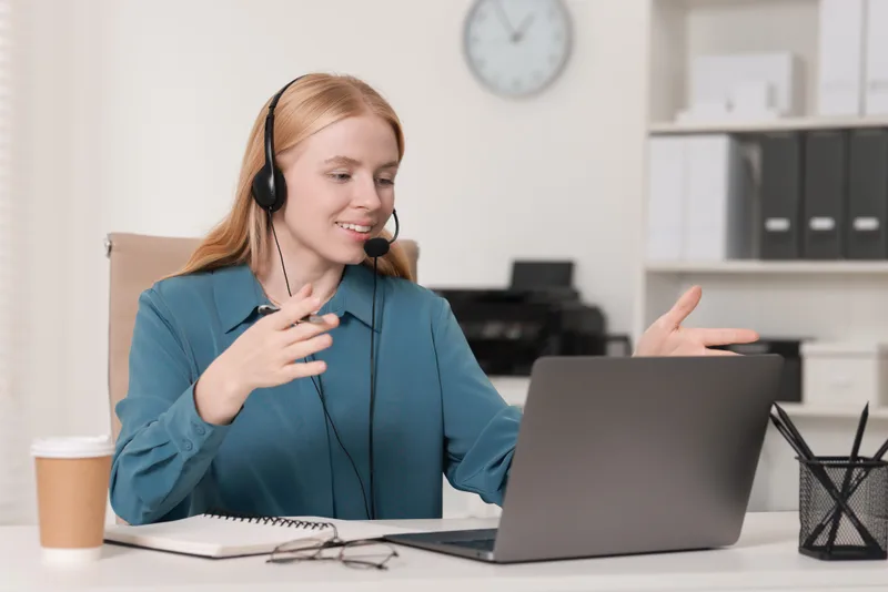 A smiling intake specialist wearing a headset talks with a caller at her desk