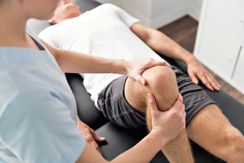 A physical therapist works on a patient's knee on a treatment table