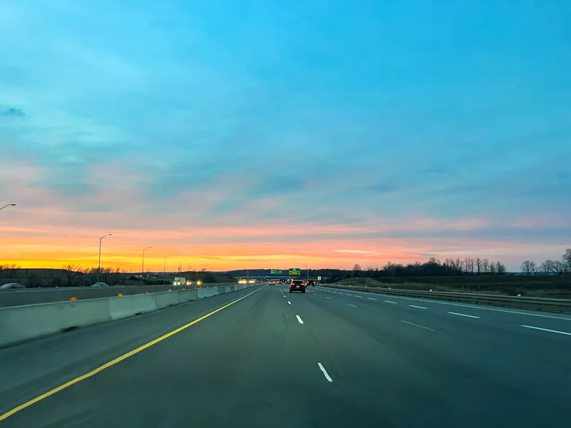 An open highway at dusk with a pink and orange sky over the lanes