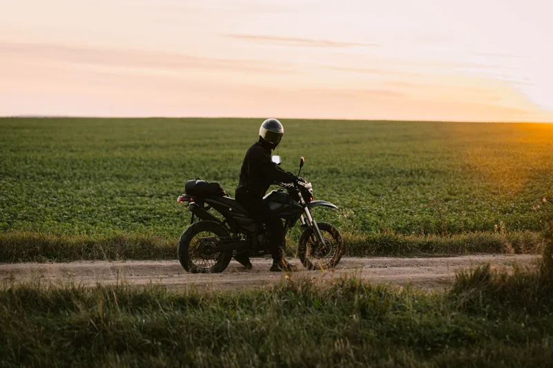 A motorcyclist riding along a quiet country road at sunset