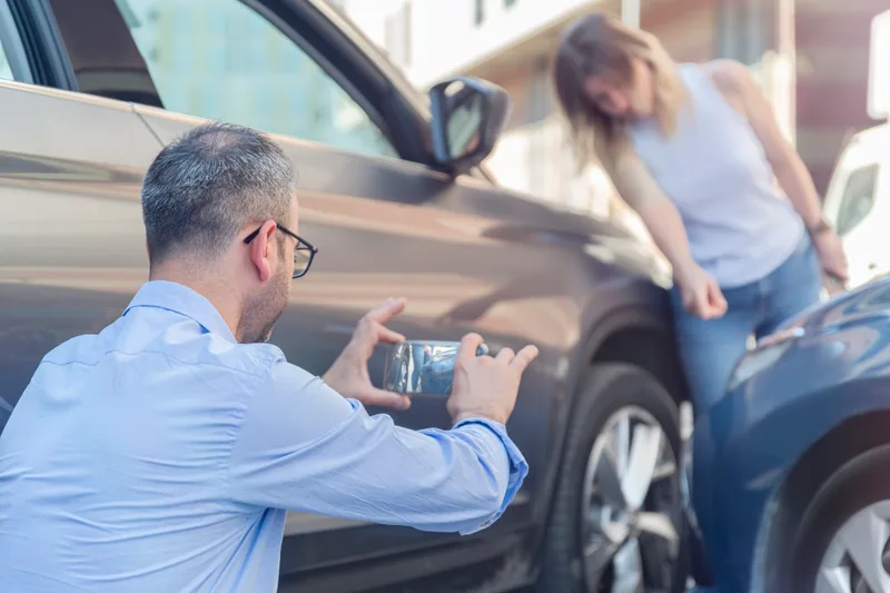 A man photographing damage to a car after a crash while the other driver looks on