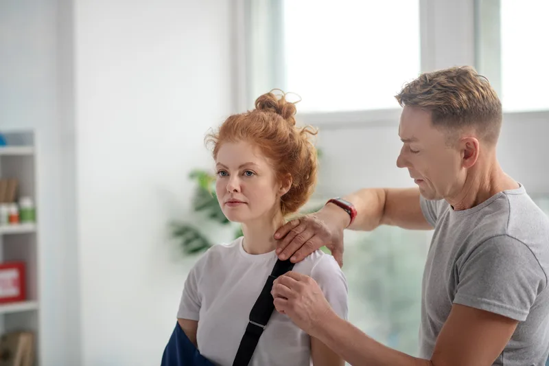 A physical therapist working on the shoulder of a patient wearing an arm sling