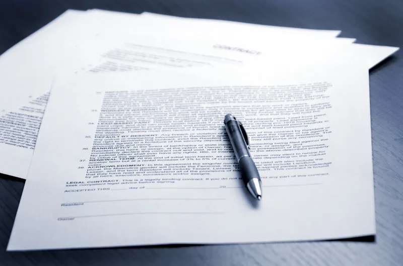 Pages of a signed agreement fanned out on a dark desk with a silver pen resting on top