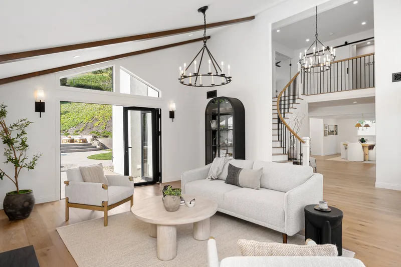 Quiet, light-filled living room with a white sofa, a round coffee table, an iron chandelier and a curved staircase behind