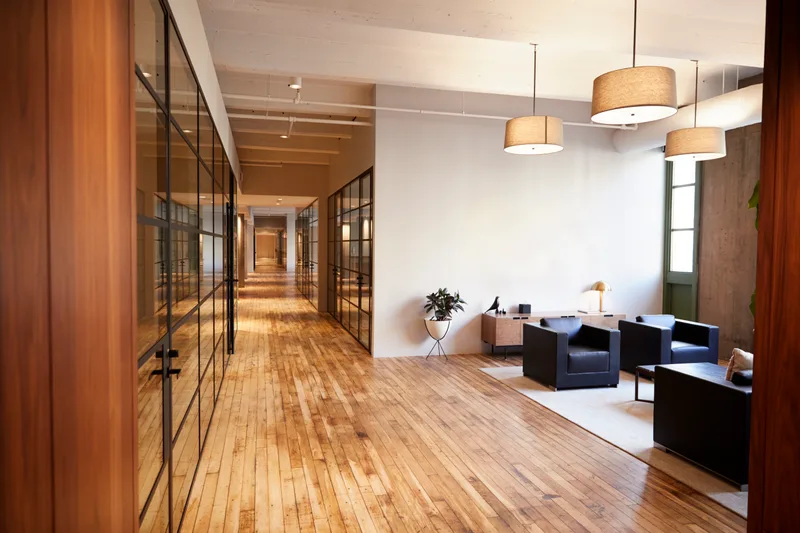 The firm's reception lounge: a long wood-floored corridor with glass-walled offices and leather armchairs under pendant lamps