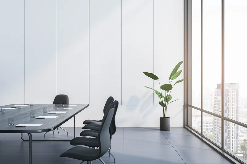 A private meeting room with a long table, black chairs, a single plant and floor-to-ceiling windows over the city