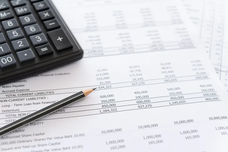 Printed balance sheet and spreadsheet pages with a pencil and a calculator