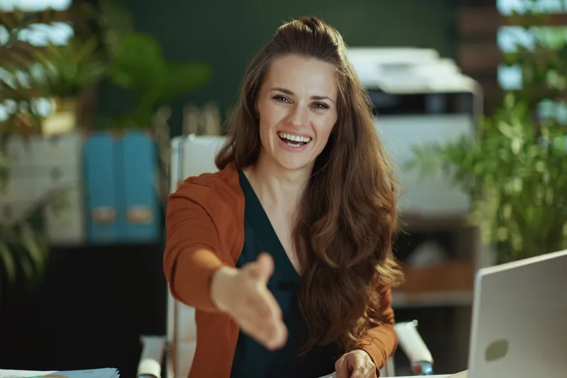 A smiling business owner reaches across her desk to shake hands