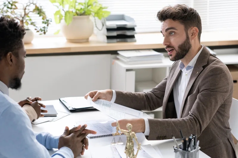 Attorney talking through paperwork with a client across a bright office desk