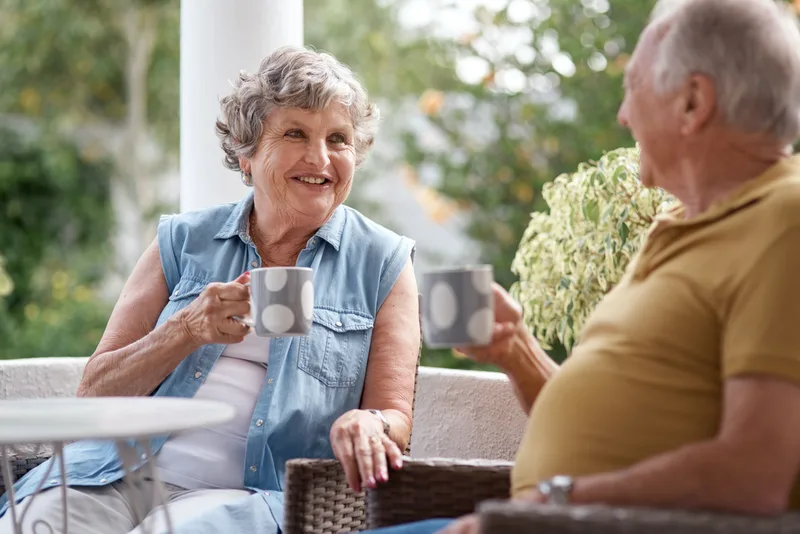 An older couple sharing coffee and a laugh on their garden patio