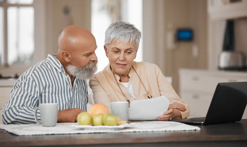A couple reading their trust papers together at the kitchen table, mugs of coffee beside them