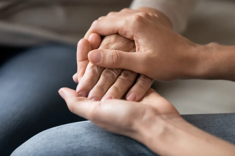 A younger woman gently holding her older mother's hand