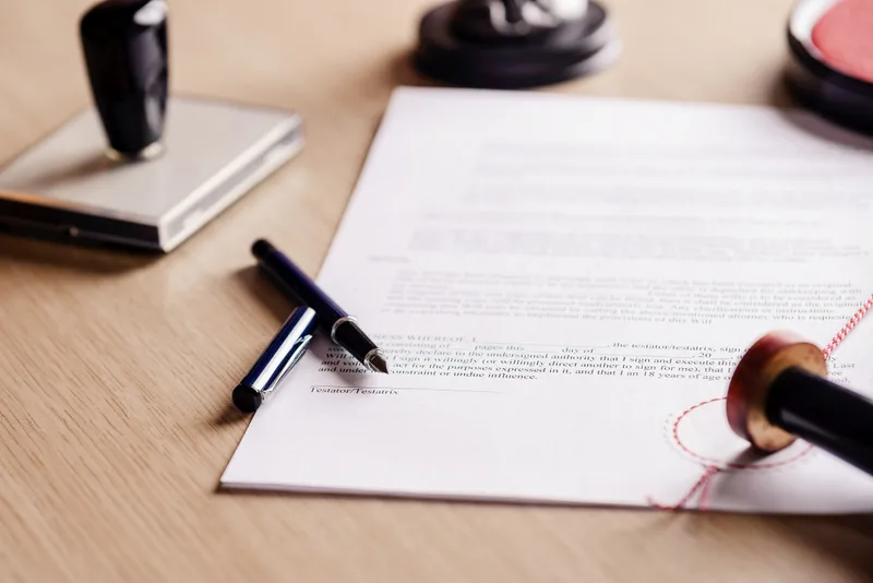 A pen resting on a signed testament beside a notary stamp