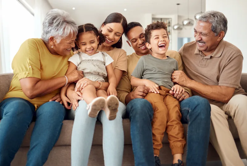 Three generations of one family laughing together on a sofa