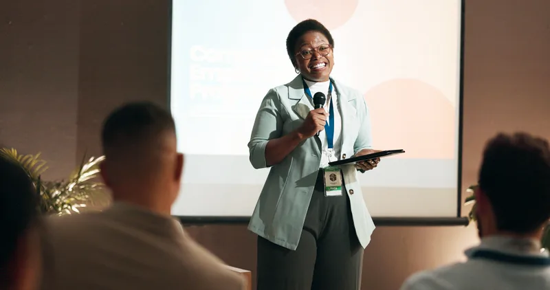 A presenter with a microphone speaking to a small seated audience at a community workshop