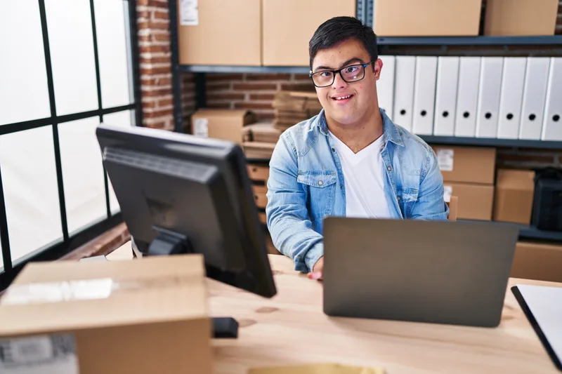 A young man with Down syndrome smiling at his desk at work