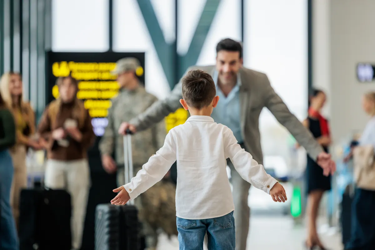 A young boy runs with open arms toward his father in an airport arrivals hall