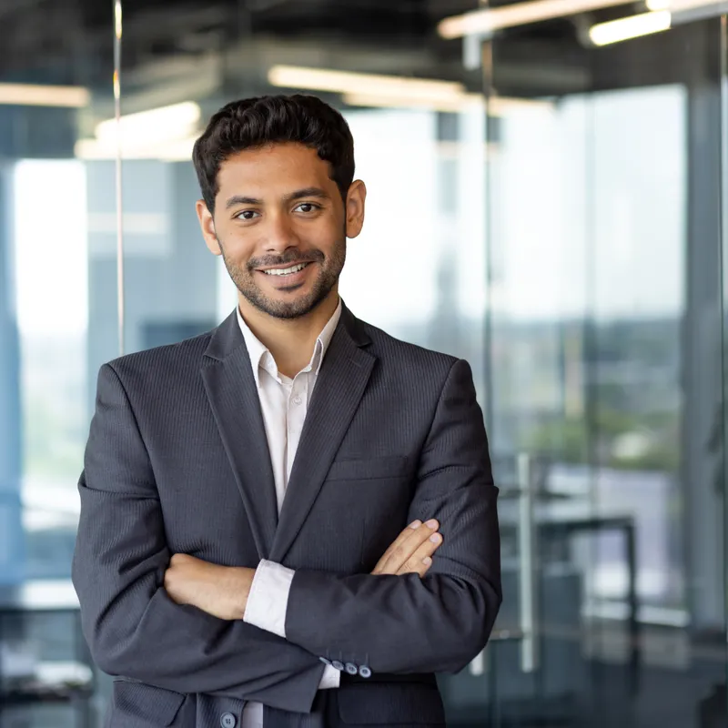 Omar El-Amine, a lawyer in a charcoal suit, smiling with his arms crossed in a glass-walled office