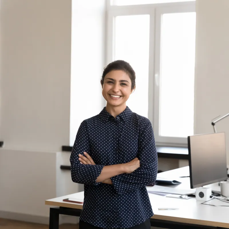 Nadia Rahman, a lawyer in a navy polka-dot blouse, smiling with her arms crossed in a bright office