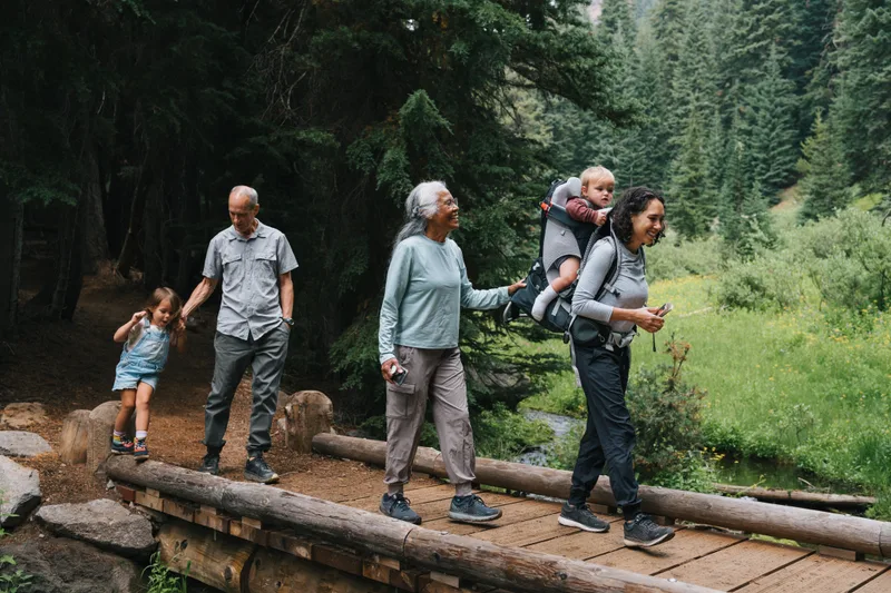 Three generations of a family cross a wooden footbridge together on a forest trail