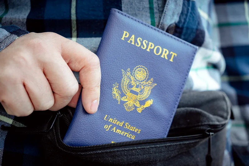 A hand slips a blue United States passport into a travel bag