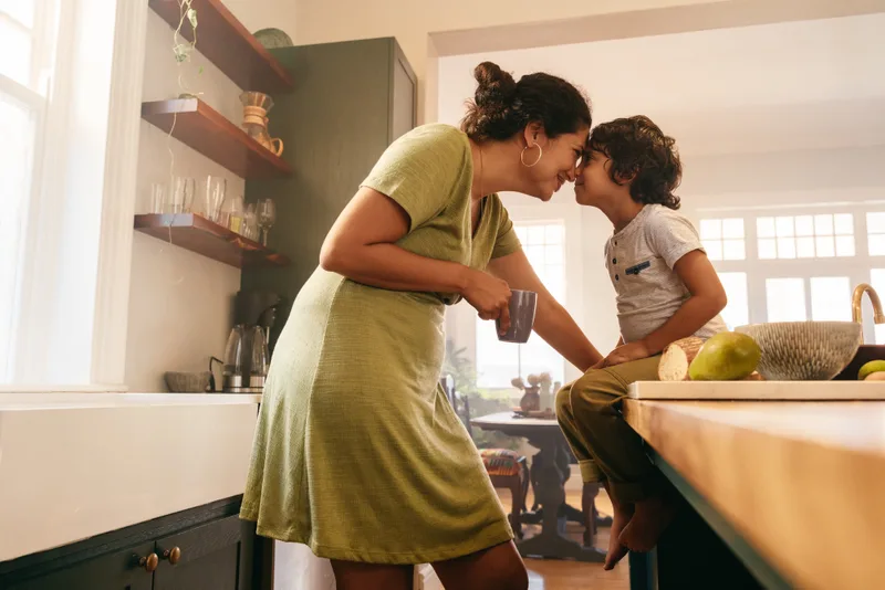 A parent and young child touching noses in a sunny kitchen