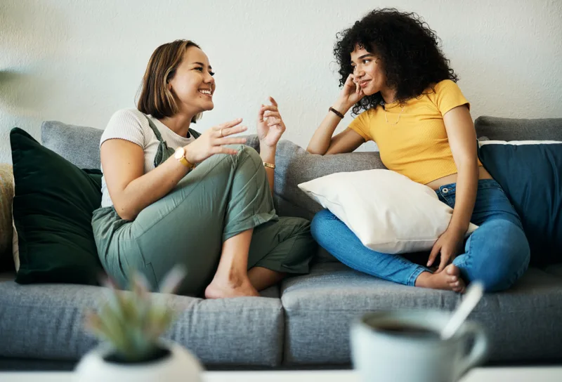 Two women talking and laughing on a sofa at home
