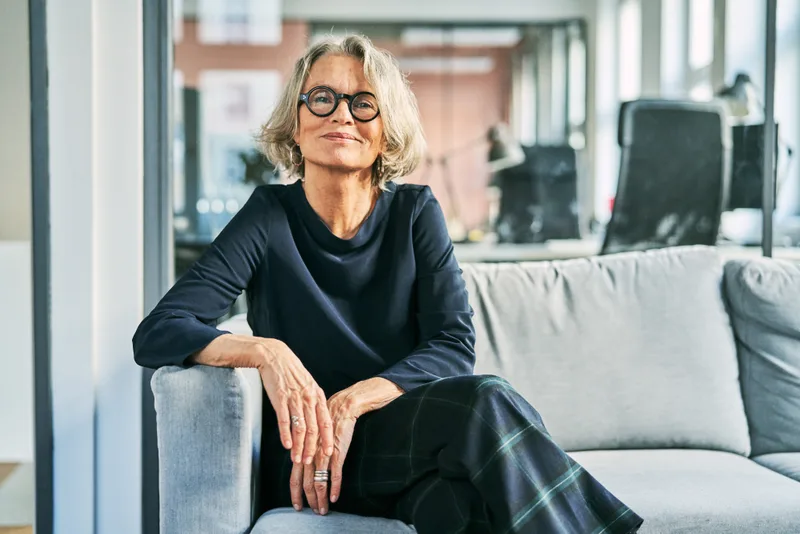 Eleanor Langford, a smiling attorney with silver hair and dark glasses, seated in the firm's office