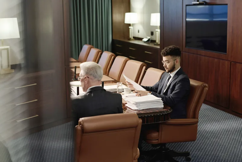 Two attorneys review case files at a long table in a wood-paneled conference room