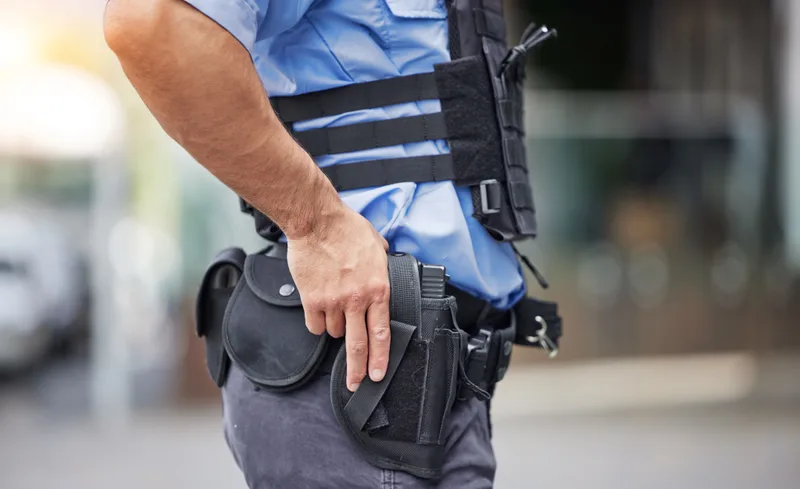 A uniformed officer rests his hand on a holstered handgun at his belt