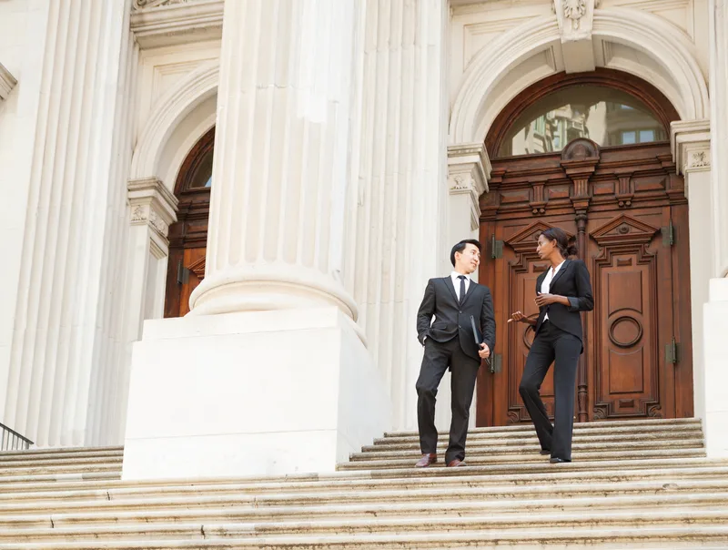 A defense attorney and her client talk as they walk down the stone steps of a columned courthouse