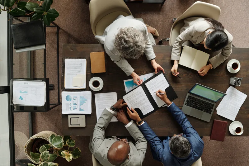 Seen from above, four colleagues review documents around a meeting table