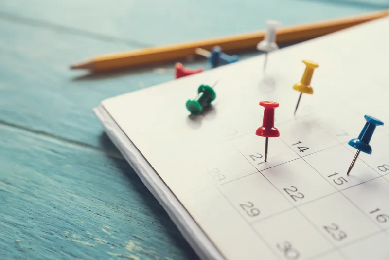A paper calendar with several dates marked by colored pins