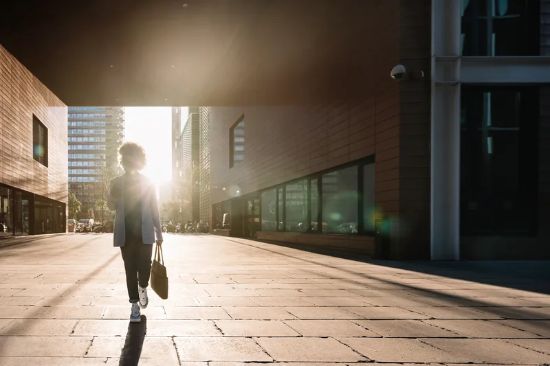 A professional walks alone with a briefcase between city buildings in early morning light