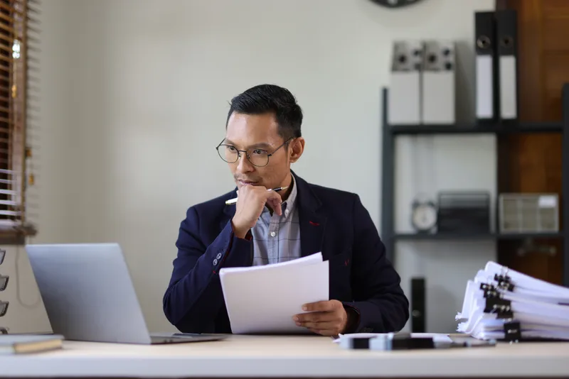 A man in a suit reads a letter at his office desk